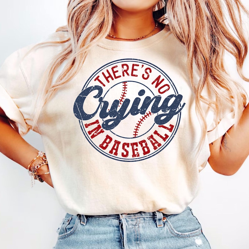 May include: A white t-shirt with a blue and red circle graphic that says "There's No Crying In Baseball".