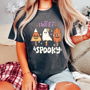 May include: Dark gray t-shirt with the words "Sweet & Spooky" and illustrations of Halloween-themed popsicles. The popsicles include a candy corn, a ghost, and a pumpkin. The shirt is a comfortable, casual style.