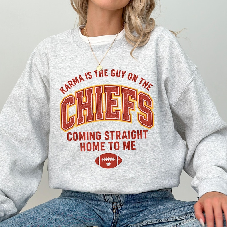 May include: A light gray sweatshirt with the text "Karma is the Guy on the Chiefs Coming Straight Home to Me" in red and gold lettering. A football graphic is below the text.