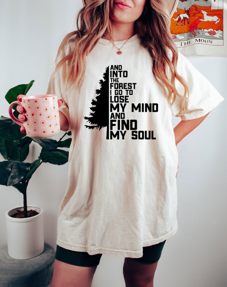 K&ouml;nnte beinhalten: Ein wei&szlig;es T-Shirt mit einer schwarzen Silhouette eines Kiefernbaums und dem Text "AND INTO THE FOREST I GO TO LOSE MY MIND AND FIND MY SOUL".