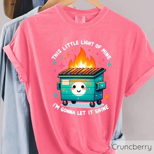 May include: Pink t-shirt with a graphic of a green dumpster on fire with the text "This little light of mine I'm gonna let it shine".