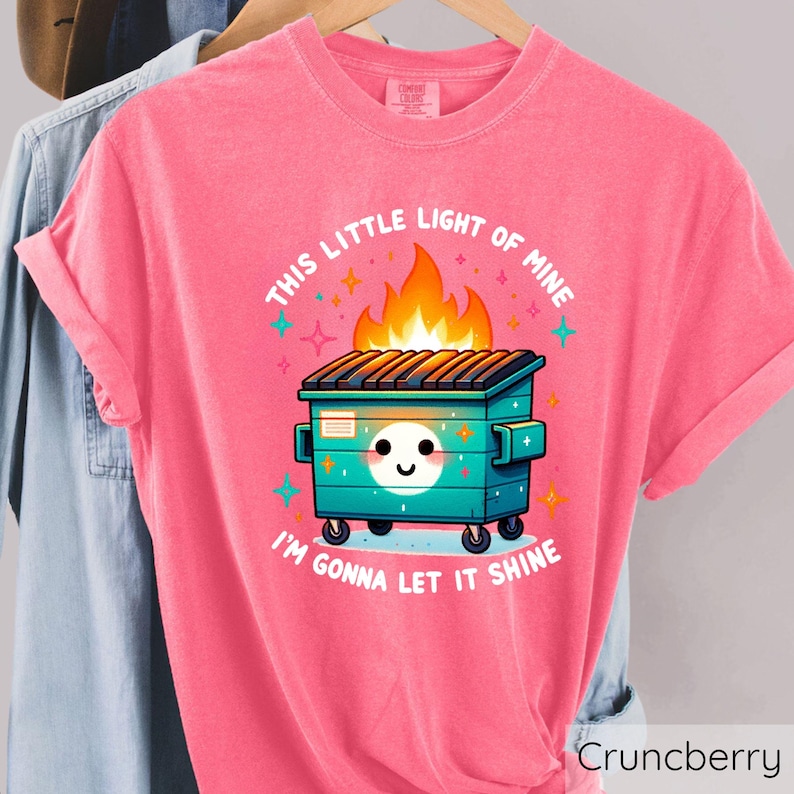 May include: Pink t-shirt with a graphic of a green dumpster on fire with the text "This little light of mine I'm gonna let it shine".