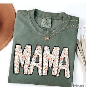 May include: A green t-shirt with a floral print "MAMA" design. The shirt has a distressed look and is made of a soft, comfortable fabric.