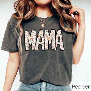 May include: A dark gray t-shirt with a floral print design that spells out "MAMA".