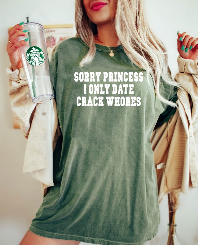 May include: A green t-shirt with the text "SORRY PRINCESS I ONLY DATE CRACK WHORE" printed in white.