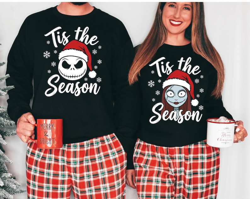 Pode incluir: Camisas pretas de manga comprida com o texto "Tis the Season" e desenhos de Jack Skellington e Sally, combinadas com cal&ccedil;as de pijama xadrez vermelhas. Uma caneca vermelha com texto &eacute; segurada.