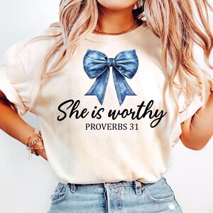 May include: A white t-shirt with a blue denim bow and the text "She is worthy Proverbs 31" printed on it.