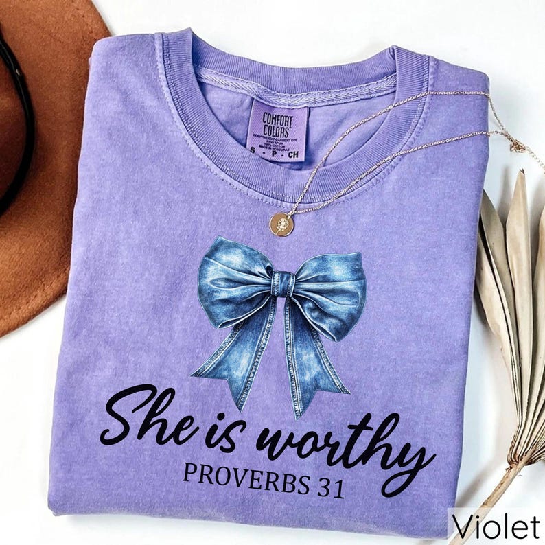 May include: A purple t-shirt with a blue denim bow and the text "She is worthy Proverbs 31" printed on the front.