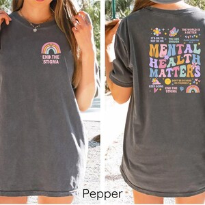 May include: A gray t-shirt with a rainbow and the text "End the Stigma" on the front. The back of the shirt has a colorful graphic with the text "Mental Health Matters" and other phrases about mental health.