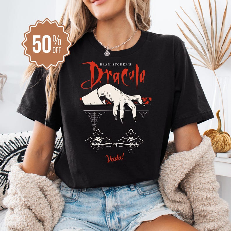 May include: Black t-shirt featuring the text "Bram Stoker's Dracula" in red, with a graphic of a hand and the word "Vudu!". A 50% off sticker is in the upper left corner. The shirt is a casual wear item.