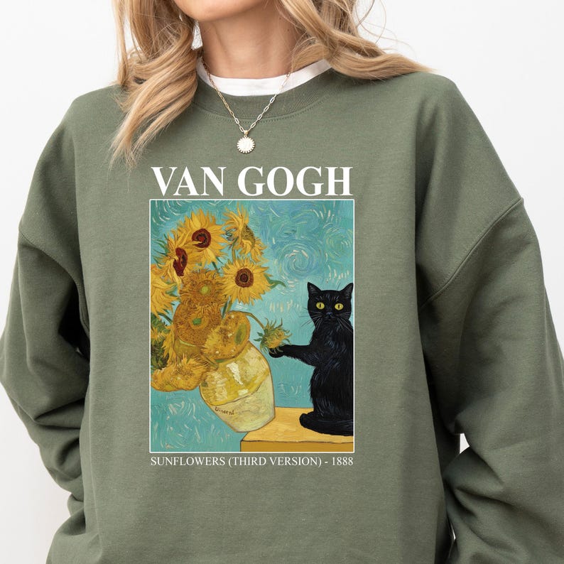 May include: Olive green sweatshirt featuring a print of Van Gogh's "Sunflowers" with a black cat. The artwork includes a vase of sunflowers and the text "VAN GOGH" and "SUNFLOWERS (THIRD VERSION) - 1888".