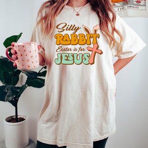 May include: A white t-shirt with a retro-style graphic that says "Silly Rabbit Easter is for Jesus" with a bunny ear and cross design.