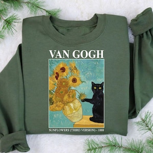 May include: Olive green sweatshirt featuring a print of Van Gogh's "Sunflowers" painting with a black cat. The print includes the text "VAN GOGH" at the top and "SUNFLOWERS (THIRD VERSION) - 1888" at the bottom.