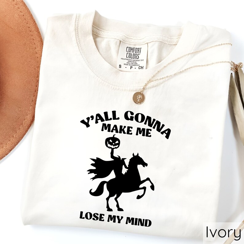 May include: A white t-shirt with a black graphic of a headless horseman riding a horse. The graphic includes the text "Y'all Gonna Make Me Lose My Mind". The shirt is labeled "Ivory".