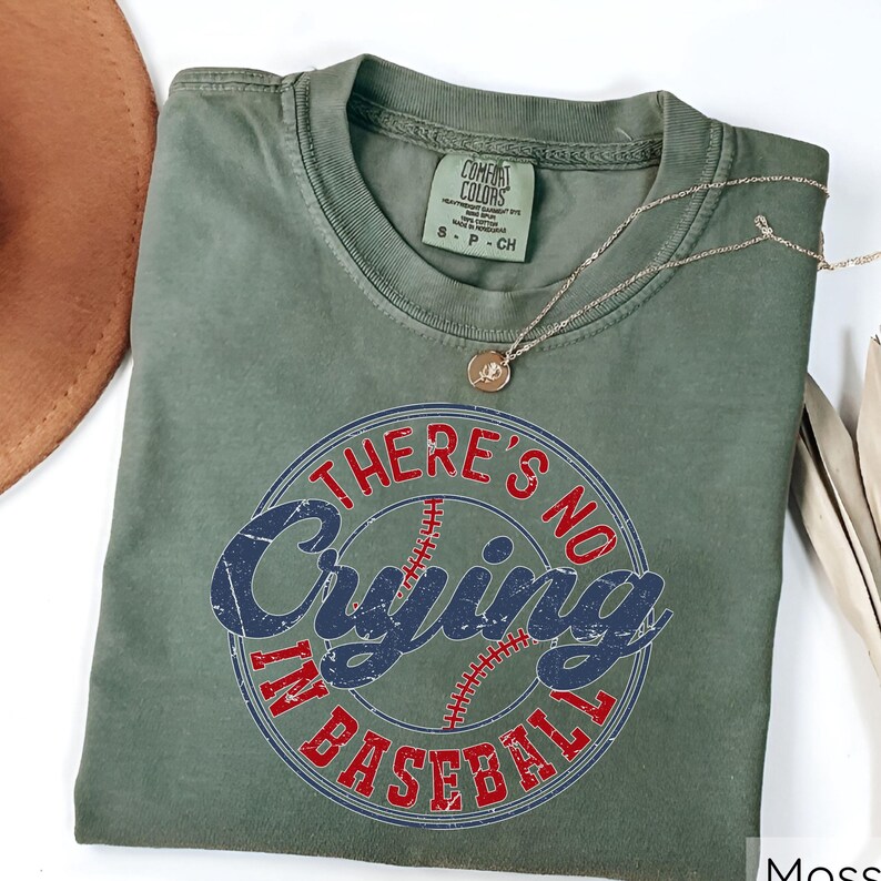 May include: Green t-shirt with a distressed, vintage-style graphic that says "There's No Crying In Baseball" with a red baseball in the center.
