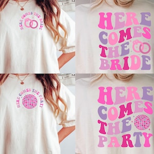 May include: Two white t-shirts with pink and purple text that reads "Here comes the bride" and "Here comes the party". One shirt features a graphic of two rings, the other a disco ball.