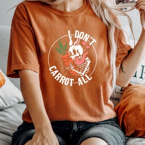 Może przedstawiać: Pomarańczowy t-shirt z nadrukiem szkieletu trzymającego marchewkę i tekstem "I don't carrot all".