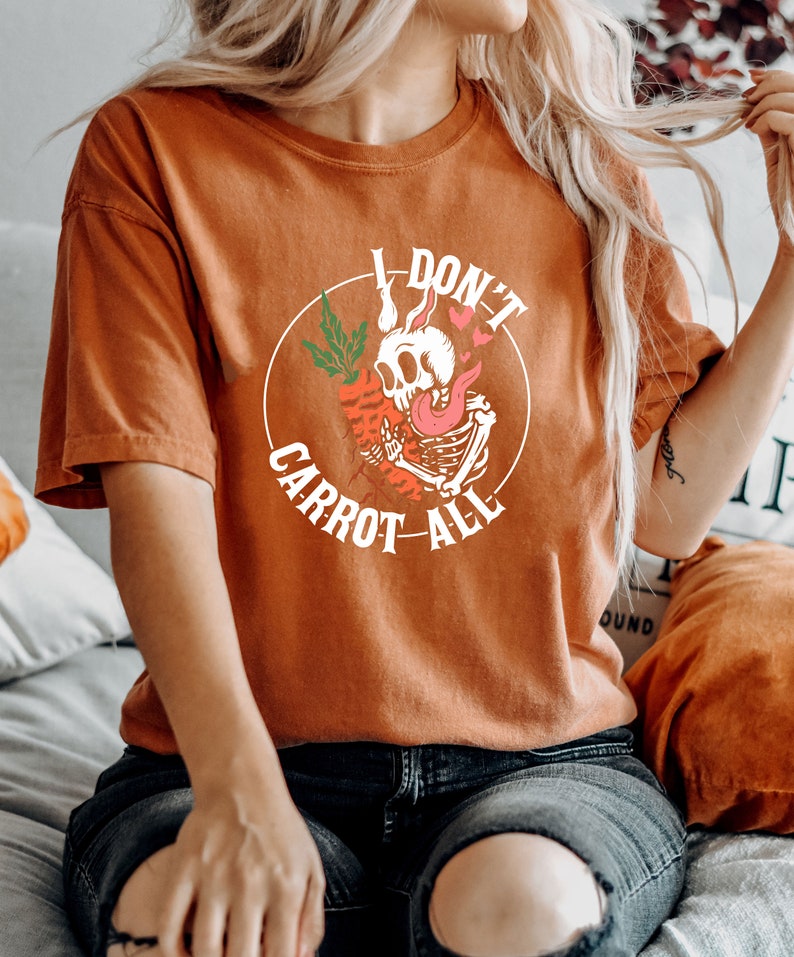 Może przedstawiać: Pomarańczowy t-shirt z nadrukiem szkieletu trzymającego marchewkę i tekstem "I don't carrot all".