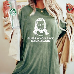 May include: Green t-shirt with a white image of Jesus and the text "GUESS WHO'S BACK BACK AGAIN".