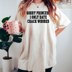 May include: A white t-shirt with the text "Sorry Princes I Only Date Crack Whores" printed in black.
