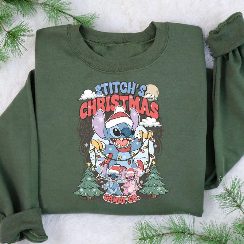 May include: Green sweatshirt featuring a graphic of Stitch in a Santa hat holding Christmas lights. The text "Stitch's Christmas Candy Co." is displayed above and below the character. Two smaller Stitch characters are also wearing Santa hats.