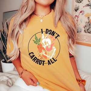 Może przedstawiać: Ż&oacute;łta koszulka z czarnym kołem graficznym przedstawiającym szkielet trzymający marchewkę i tekst "I Don't Carrot All".