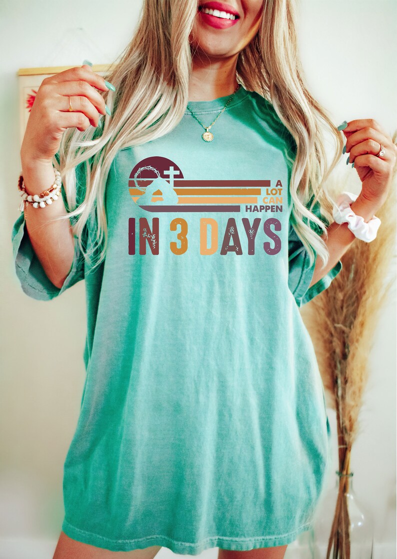 Może przedstawiać: Turkusowy t-shirt z nadrukiem graficznym przedstawiającym kości&oacute;ł z krzyżem, zach&oacute;d słońca i tekst "A lot can happen in 3 days".