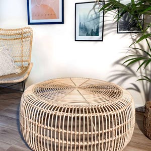 May include: A round, natural-toned rattan coffee table. The table has a woven top and vertical supports, creating an open, airy design. The table is approximately 30 inches in diameter and 16 inches tall, suitable for a living room or patio.