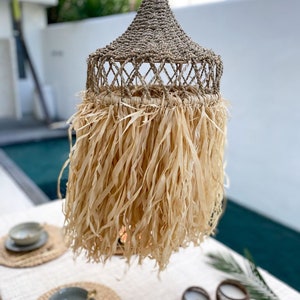 May include: A woven, natural fiber pendant light with a fringe of shredded paper. The light is hanging over a table with place settings and candles.