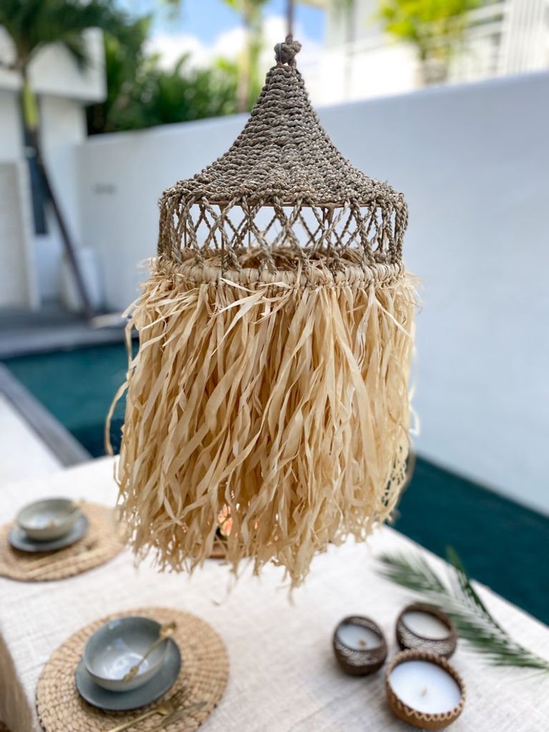 May include: A woven, natural fiber pendant light with a fringe of shredded paper. The light is hanging over a table with place settings and candles.