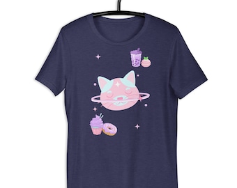 Op de afbeelding: Marineblauw T-shirt met een grillig ontwerp van een roze en blauwe kattenplaneet, omringd door sterren, een cupcake, een donut, bubble tea en een macaron. Het ontwerp is speels.