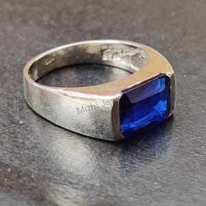 May include: A silver ring with a rectangular, deep blue gemstone. The ring has a simple, modern design with a polished finish. The ring is likely made of sterling silver and is suitable for everyday wear.
