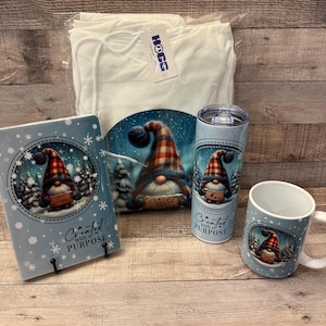 May include: A gift set featuring a white hoodie, a blue and white ceramic mug, a blue and white tumbler, and a blue and white journal with a gnome design. The journal has the text "Created with a PURPOSE" on the front. The mug and tumbler also have the text "Created with a PURPOSE" on them.