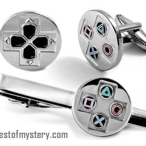 Può includere: Un set di gemelli e una clip per cravatta argentati con un design stilizzato di controller per videogiochi. I pulsanti del controller sono colorati di blu, rosa, rosso e verde.