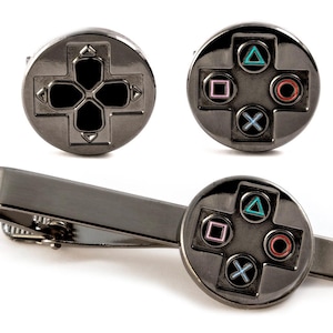 Puede incluir: Un conjunto de accesorios en tono gris plomo que incluye dos gemelos circulares y un pasador de corbata. Las piezas presentan un diseño de cruceta direccional y los símbolos clásicos de juego: triángulo, círculo, cuadrado y cruz.
