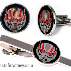 May include: A silver tie clip and cufflinks set featuring a black and red Ant-Man character design.