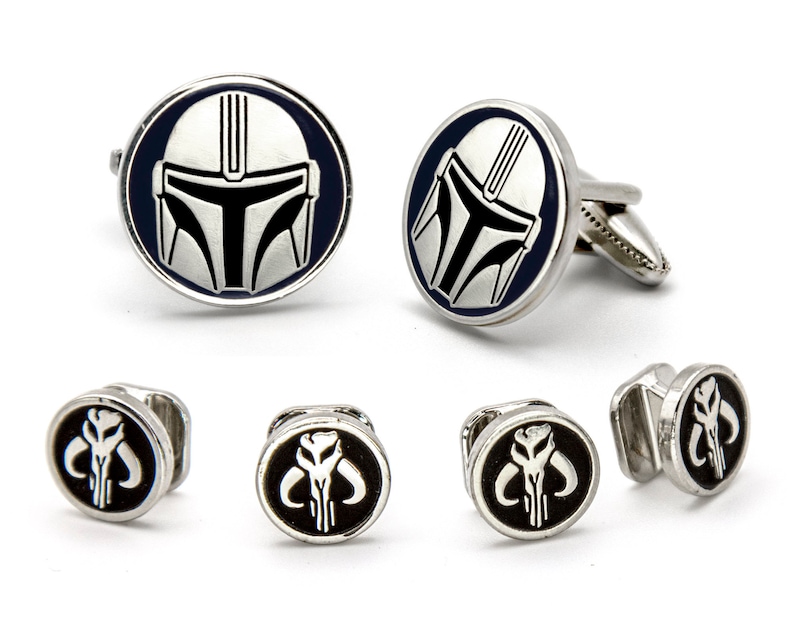 May include: A set of cufflinks and tie tacks featuring the Mandalorian's helmet and symbol. The cufflinks are silver with a blue background and the tie tacks are silver with a black background.