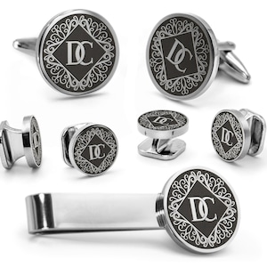 May include: A set of silver-toned cufflinks, shirt studs, and a tie clip. Each piece features a black circular face with a white decorative border and the initials "DC" in a diamond shape.
