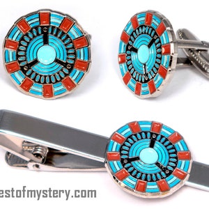 May include: A set of silver cufflinks and a tie clip featuring a circular design with a blue and red pattern. The design resembles a futuristic target or a circuit board.