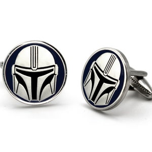 May include: A pair of silver cufflinks with a blue enamel background and a white and black Mandalorian helmet design.