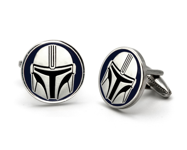 May include: A pair of silver cufflinks with a blue enamel background and a white and black Mandalorian helmet design.