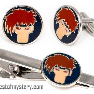 May include: A set of cufflinks and a tie clip featuring a cartoon portrait of a character with red hair and red eyes. The character's face is on a blue background with a silver border.