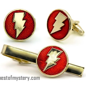 May include: A set of three gold-toned cufflinks and a tie clip featuring a red enamel background with a yellow lightning bolt design.
