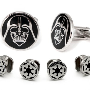 May include: A set of silver-toned metal cufflinks featuring a black and silver circular design of a helmeted character face, alongside four smaller silver-toned metal shirt studs with a black and silver circular Imperial emblem design.