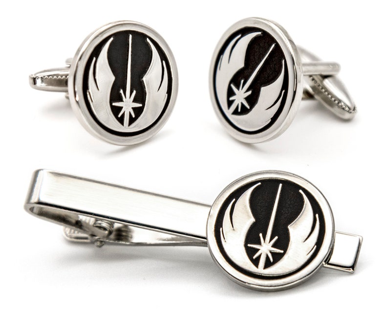 May include: A set of silver cufflinks and a tie bar featuring the Rebel Alliance symbol from Star Wars. The symbol is black and white with a lightsaber in the centre.