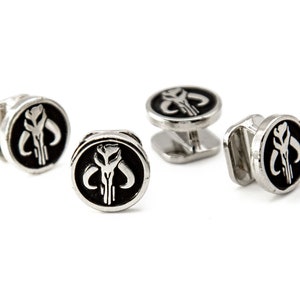 May include: Four silver cufflinks with a black enamel Mandalorian symbol. The symbol is a white skull with horns.