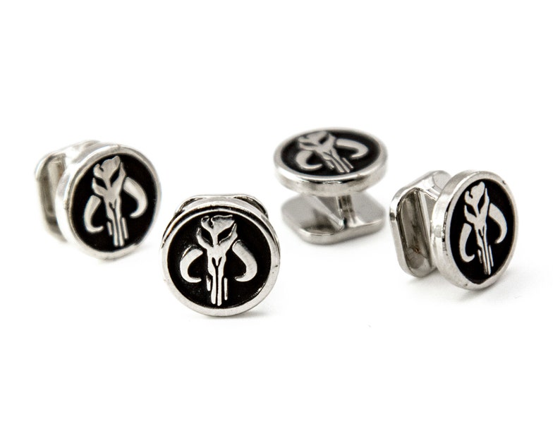 May include: Four silver cufflinks with a black enamel Mandalorian symbol. The symbol is a white skull with horns.