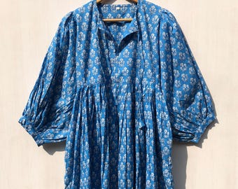 Puede incluir: Un vestido de algodón azul con estampado floral blanco y falda fruncida. El vestido tiene un escote en V y mangas 3/4.