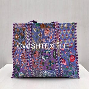 May include: A rectangular quilted tote bag featuring a vibrant purple base with a multi-colored floral print. The bag includes two matching fabric handles and vertical striped piping along the edges. The text WISHTEXTILE is printed in white.
