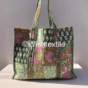 May include: A quilted tote bag featuring a patchwork design of green, pink, and white floral and leaf patterns. The bag has two matching quilted handles and vertical striped piping along the seams. The text "©Wishtextile" is printed in white.